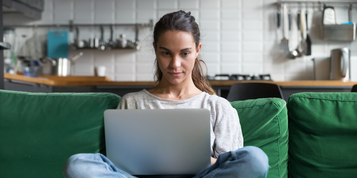 Woman remote working on laptop with legs crossed on sofa